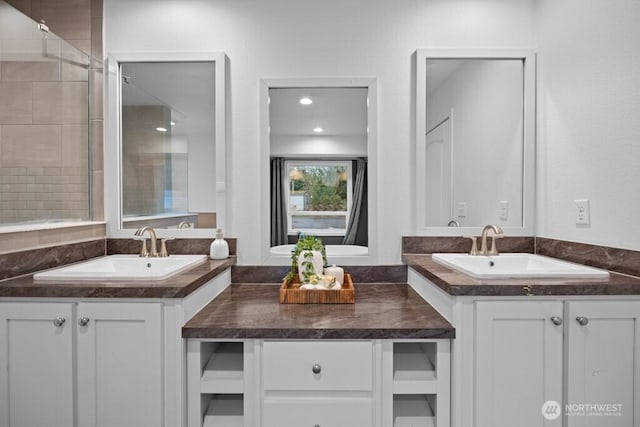 bathroom with a tile shower, two vanities, and a sink