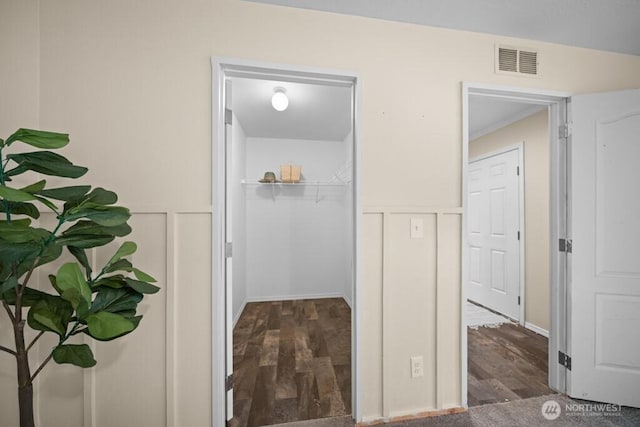 hallway with a wainscoted wall, visible vents, a decorative wall, and wood finished floors