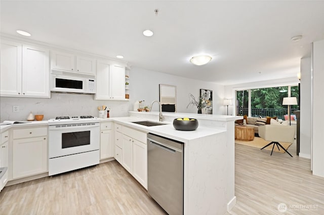 kitchen featuring a sink, white cabinetry, white appliances, light wood-style floors, and a peninsula