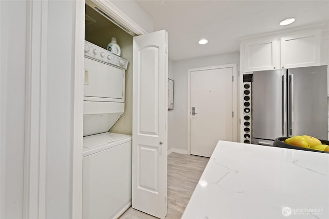 laundry area featuring baseboards, light wood-type flooring, stacked washer and dryer, laundry area, and recessed lighting