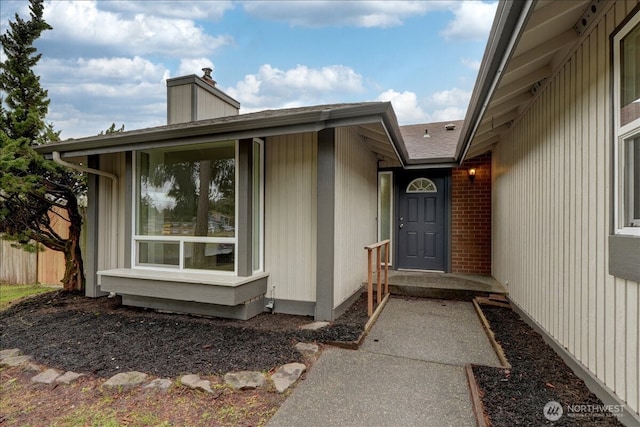 view of exterior entry featuring brick siding, a chimney, and fence