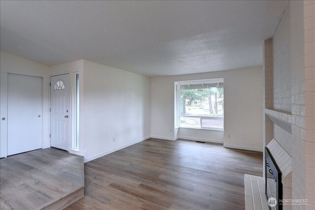 unfurnished living room featuring visible vents, a textured ceiling, wood finished floors, baseboards, and a brick fireplace