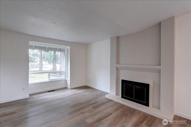 unfurnished living room with visible vents, a brick fireplace, baseboards, wood finished floors, and a textured ceiling