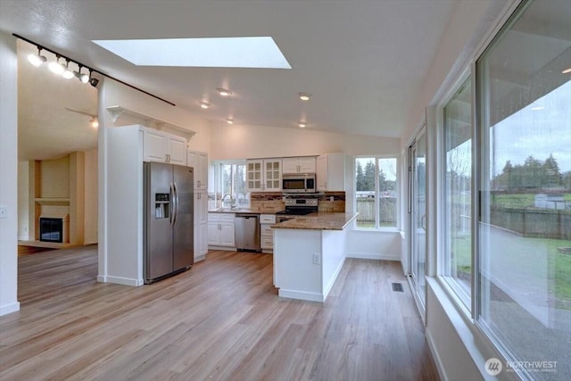 kitchen with lofted ceiling with skylight, white cabinetry, appliances with stainless steel finishes, a peninsula, and glass insert cabinets