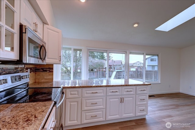 kitchen featuring light stone counters, stainless steel appliances, decorative backsplash, white cabinets, and light wood-type flooring