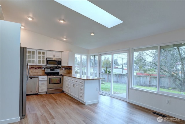 kitchen featuring visible vents, vaulted ceiling with skylight, a peninsula, white cabinets, and stainless steel appliances