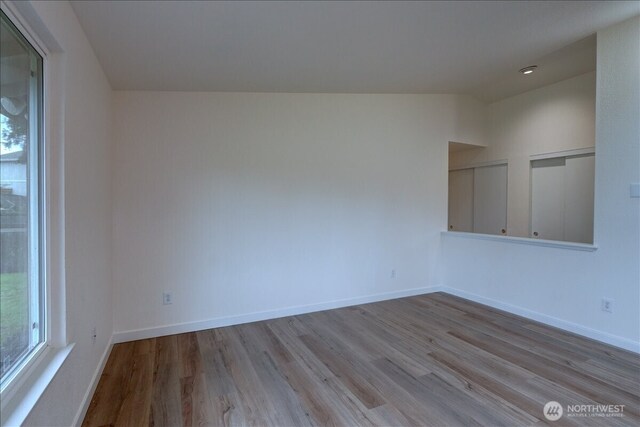 unfurnished room featuring plenty of natural light, lofted ceiling, baseboards, and wood finished floors