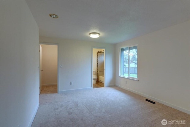 unfurnished bedroom featuring visible vents, baseboards, carpet floors, ensuite bathroom, and a walk in closet