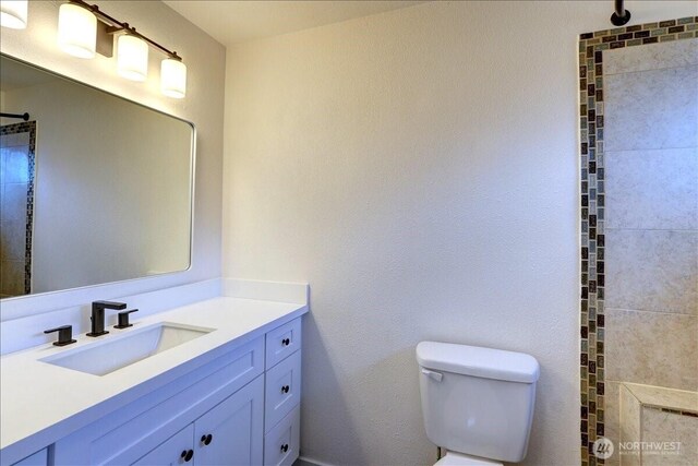 full bathroom with tiled shower, toilet, and vanity