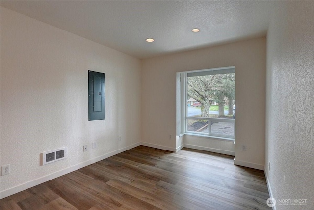 spare room featuring electric panel, visible vents, baseboards, and wood finished floors