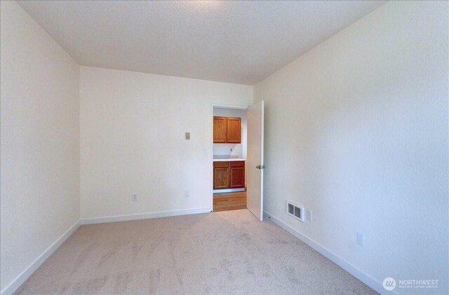 spare room featuring light carpet and baseboards