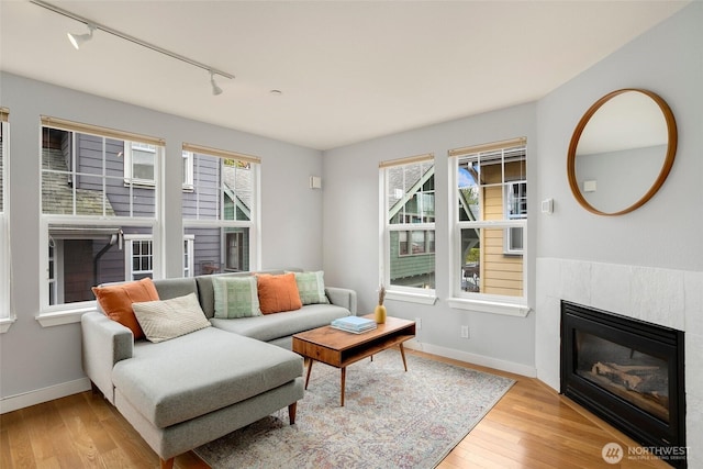 living area featuring a fireplace, baseboards, track lighting, and wood finished floors