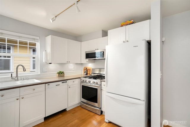 kitchen featuring appliances with stainless steel finishes, a sink, light wood-style floors, and white cabinets