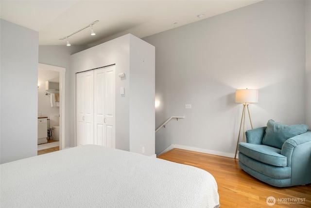 bedroom with light wood-type flooring, ensuite bath, baseboards, and a closet