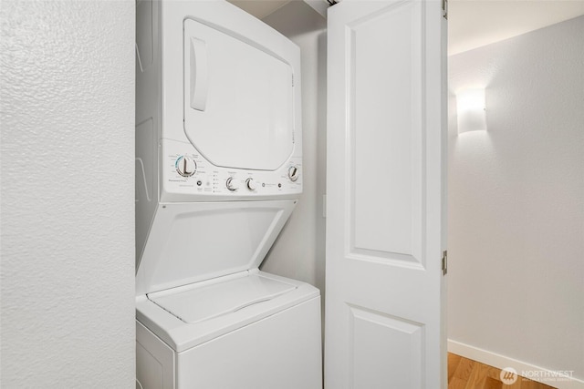 laundry room with light wood-style floors, laundry area, baseboards, and stacked washing maching and dryer