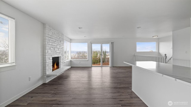 unfurnished living room featuring a fireplace, dark wood-type flooring, a healthy amount of sunlight, and baseboards