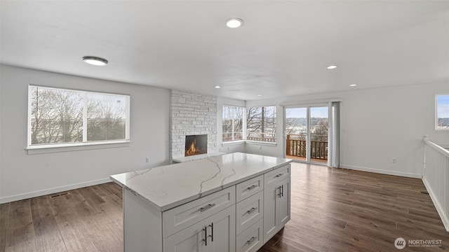 kitchen with light stone counters, open floor plan, dark wood finished floors, and a fireplace