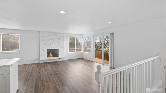 unfurnished living room with a stone fireplace, recessed lighting, wood finished floors, and baseboards