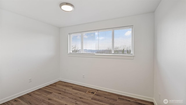 unfurnished room featuring visible vents, dark wood-type flooring, and baseboards