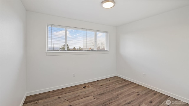 spare room featuring visible vents, baseboards, and wood finished floors