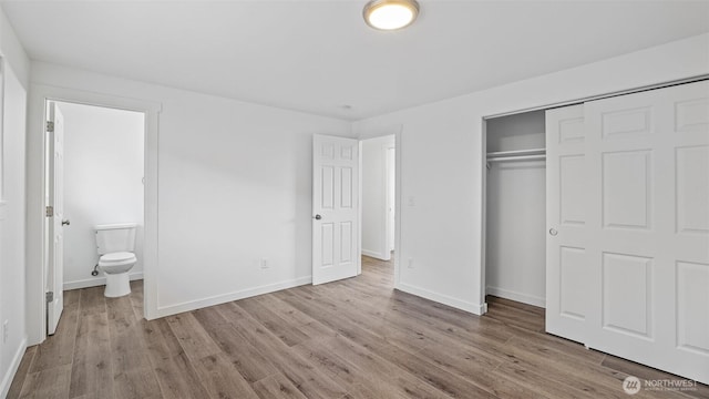 unfurnished bedroom featuring a closet, baseboards, ensuite bath, and wood finished floors