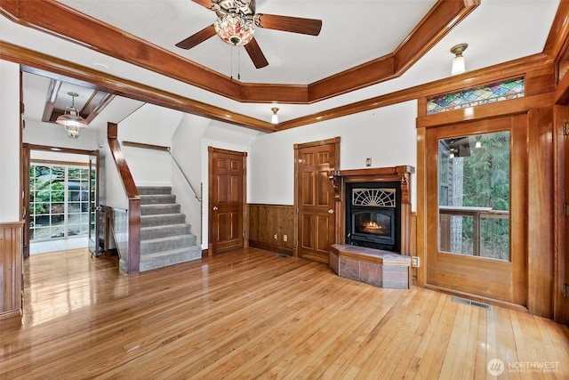 unfurnished living room featuring a wainscoted wall, wood-type flooring, visible vents, stairway, and a glass covered fireplace