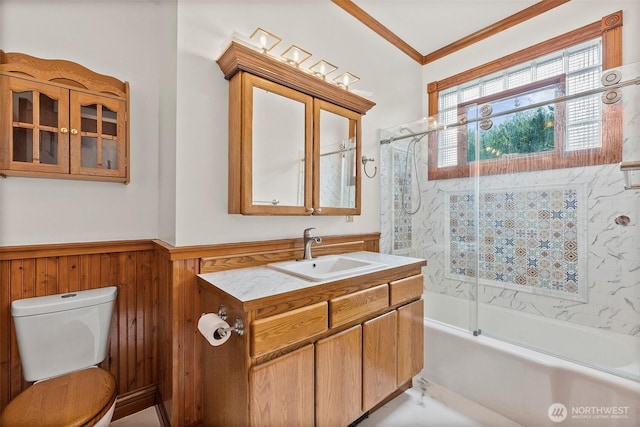 full bathroom with toilet, a wainscoted wall, combined bath / shower with glass door, crown molding, and vanity