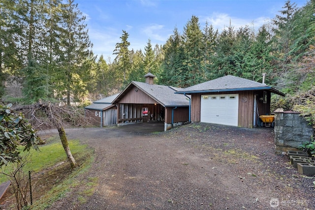 view of front of property with a shingled roof, dirt driveway, a detached garage, and an outbuilding