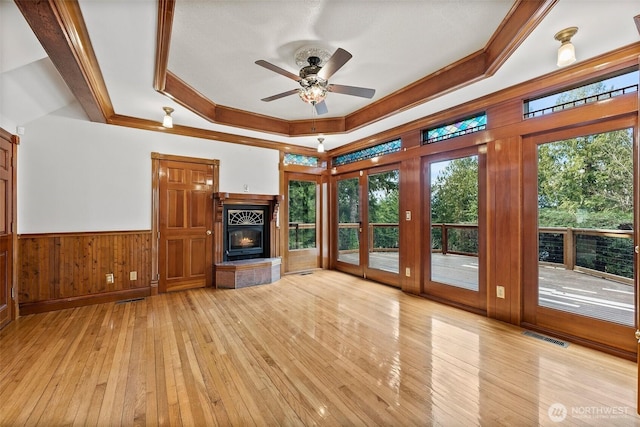 unfurnished living room with visible vents, a raised ceiling, wainscoting, crown molding, and light wood-style floors