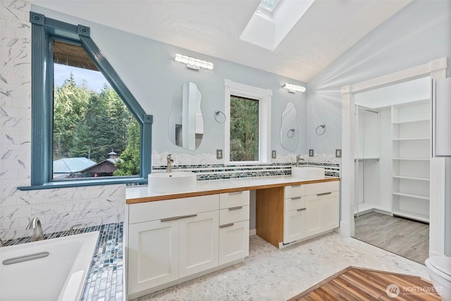 full bath featuring a soaking tub, vaulted ceiling with skylight, decorative backsplash, and vanity