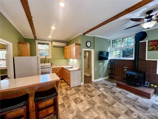 kitchen featuring a wall unit AC, light countertops, a wood stove, white appliances, and baseboards