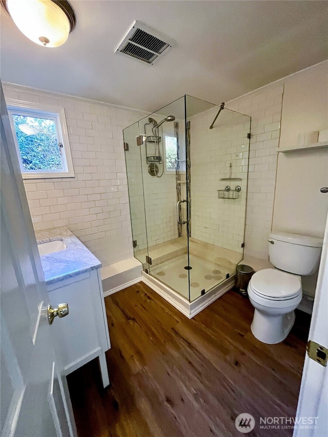 full bath featuring visible vents, toilet, vanity, a shower stall, and wood finished floors