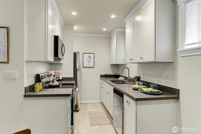 kitchen featuring appliances with stainless steel finishes, dark countertops, a sink, and white cabinetry