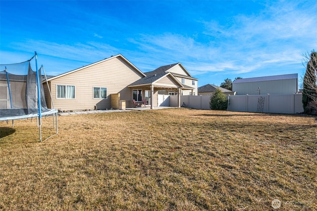 rear view of house featuring a patio area, a trampoline, fence, and a yard