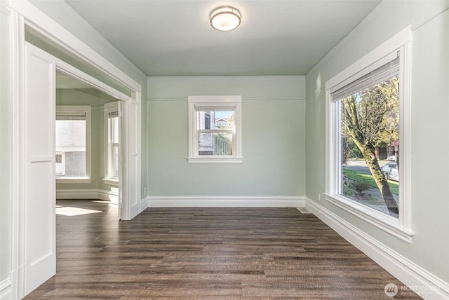 empty room featuring dark wood-style floors, a healthy amount of sunlight, and baseboards