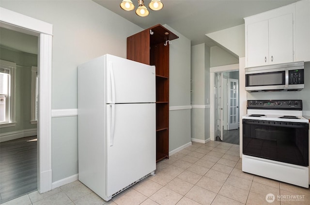 kitchen featuring light tile patterned flooring, freestanding refrigerator, electric range oven, white cabinetry, and stainless steel microwave