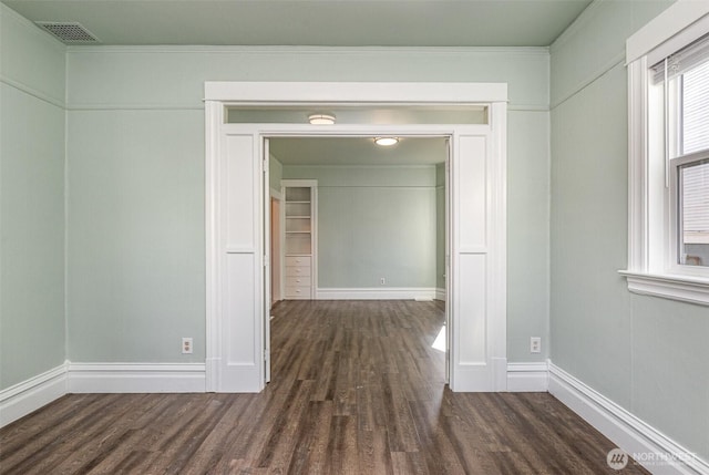 empty room featuring visible vents, dark wood-type flooring, and baseboards