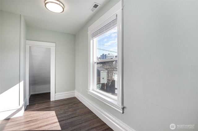 empty room featuring dark wood-style floors, visible vents, and baseboards