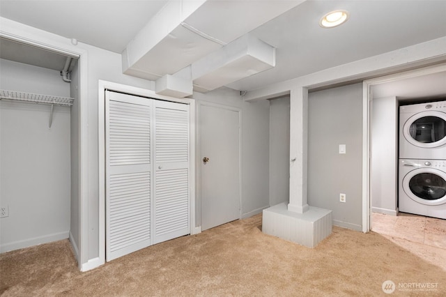 laundry area featuring laundry area, baseboards, stacked washer / drying machine, and light carpet