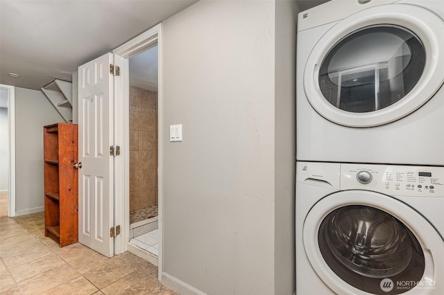 clothes washing area featuring baseboards, stacked washer and dryer, and laundry area