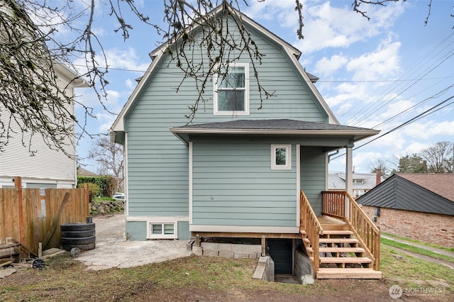 rear view of property with a gambrel roof, a shingled roof, and fence