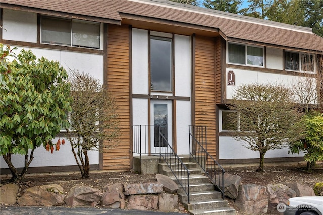 exterior space with stucco siding and a shingled roof