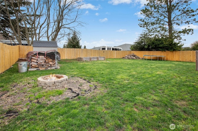 view of yard with a trampoline, an outdoor fire pit, and a fenced backyard