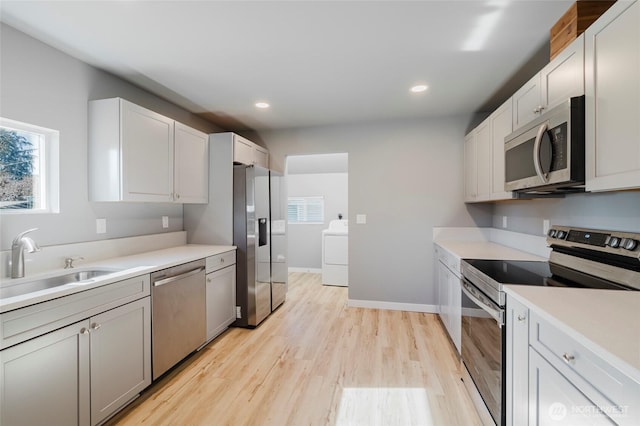 kitchen featuring plenty of natural light, washer / clothes dryer, stainless steel appliances, light wood-type flooring, and a sink