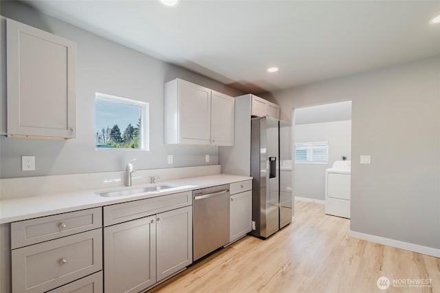 kitchen with washer / dryer, baseboards, appliances with stainless steel finishes, light wood-style floors, and a sink