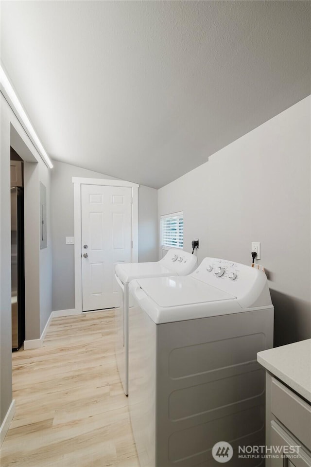 clothes washing area featuring light wood-style floors, washer and dryer, laundry area, electric panel, and baseboards