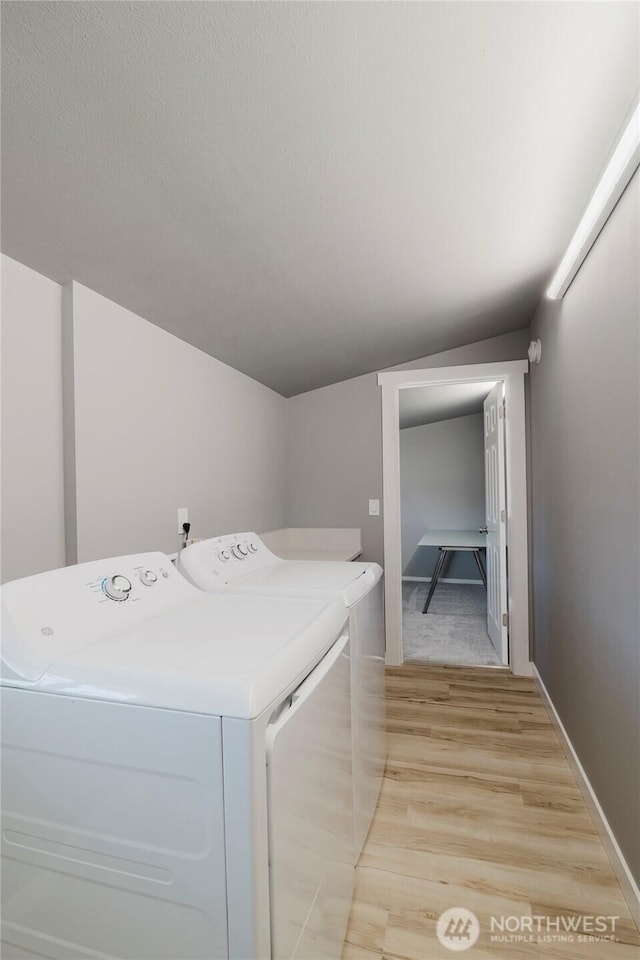 clothes washing area featuring laundry area, baseboards, separate washer and dryer, and light wood-style floors