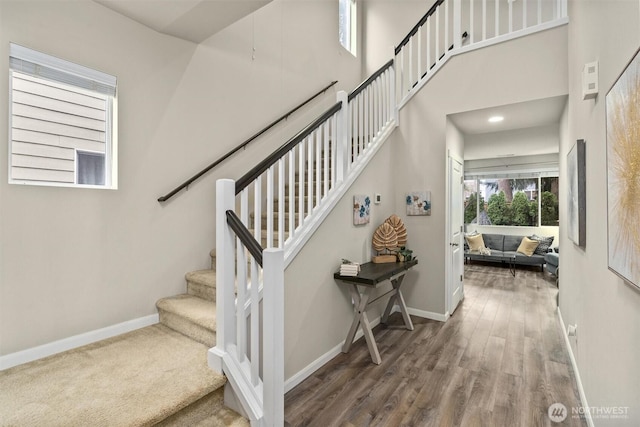 staircase with recessed lighting, a towering ceiling, baseboards, and wood finished floors