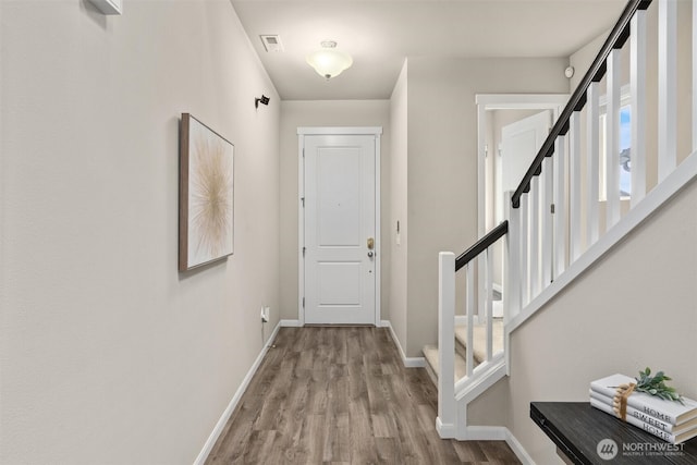 foyer featuring visible vents, stairway, baseboards, and wood finished floors