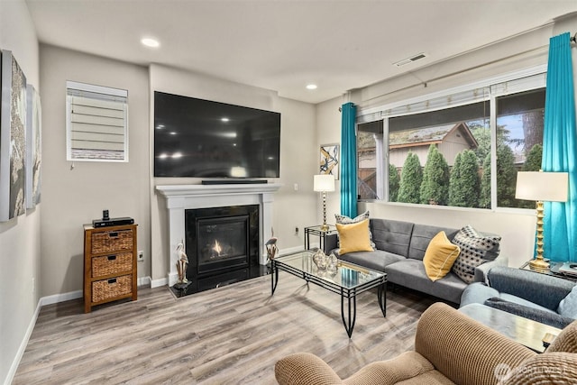 living room featuring recessed lighting, visible vents, a fireplace with flush hearth, wood finished floors, and baseboards